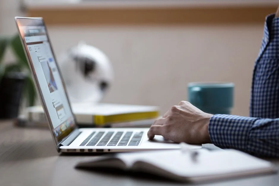 Hands using a tablet beside a laptop in a home office setting, showcasing online browsing.